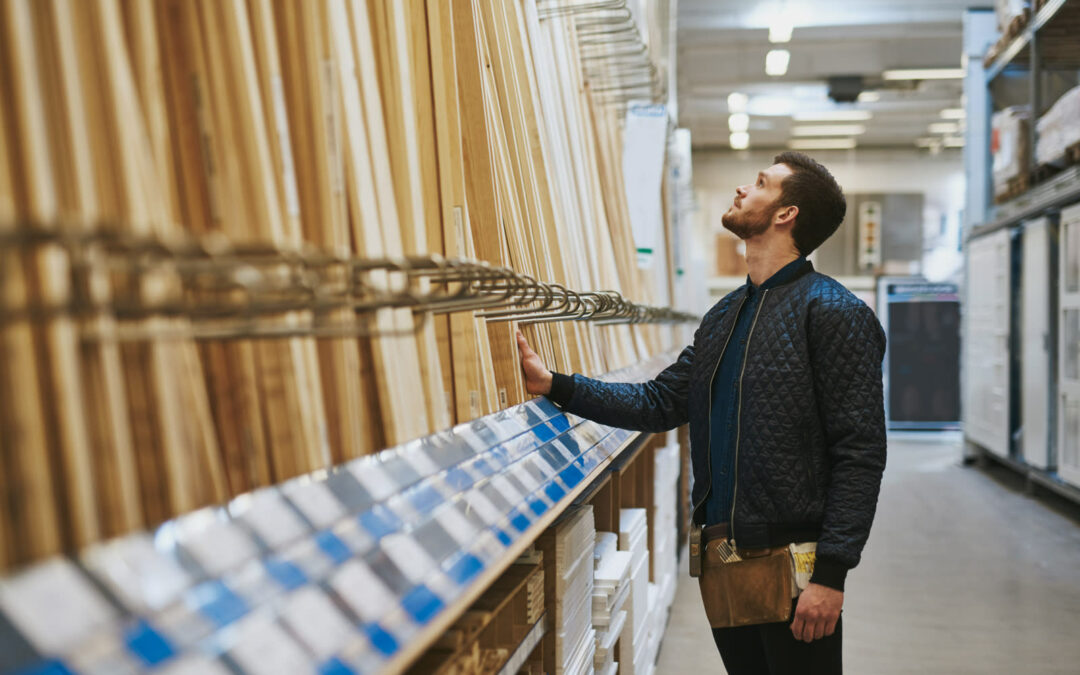 A man in a quilted jacket reaches up to a tall rack of timber lengths and moulding in the aisle of a building-supply store.